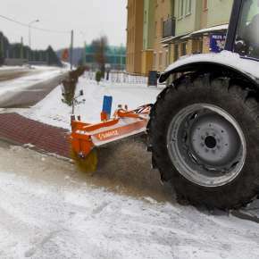Widok boczny ciągnika rolniczego z podczepioną zamiatarką MOP firmy Samasz podczas odśnieżania chodnika www.korbanek.pl