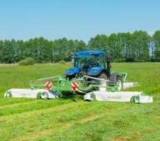 Niebieski traktor rolniczy z zestawem kosiarek MegaCUT firmy Samasz podczas koszenia trawy na łące