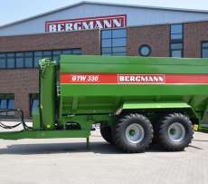 Przed budynkiem produkcyjnym firmy Bergmann stoi przyczepa do przeładunku zboża typ GTW koloru zielonego z napisem GTW Bergmann
