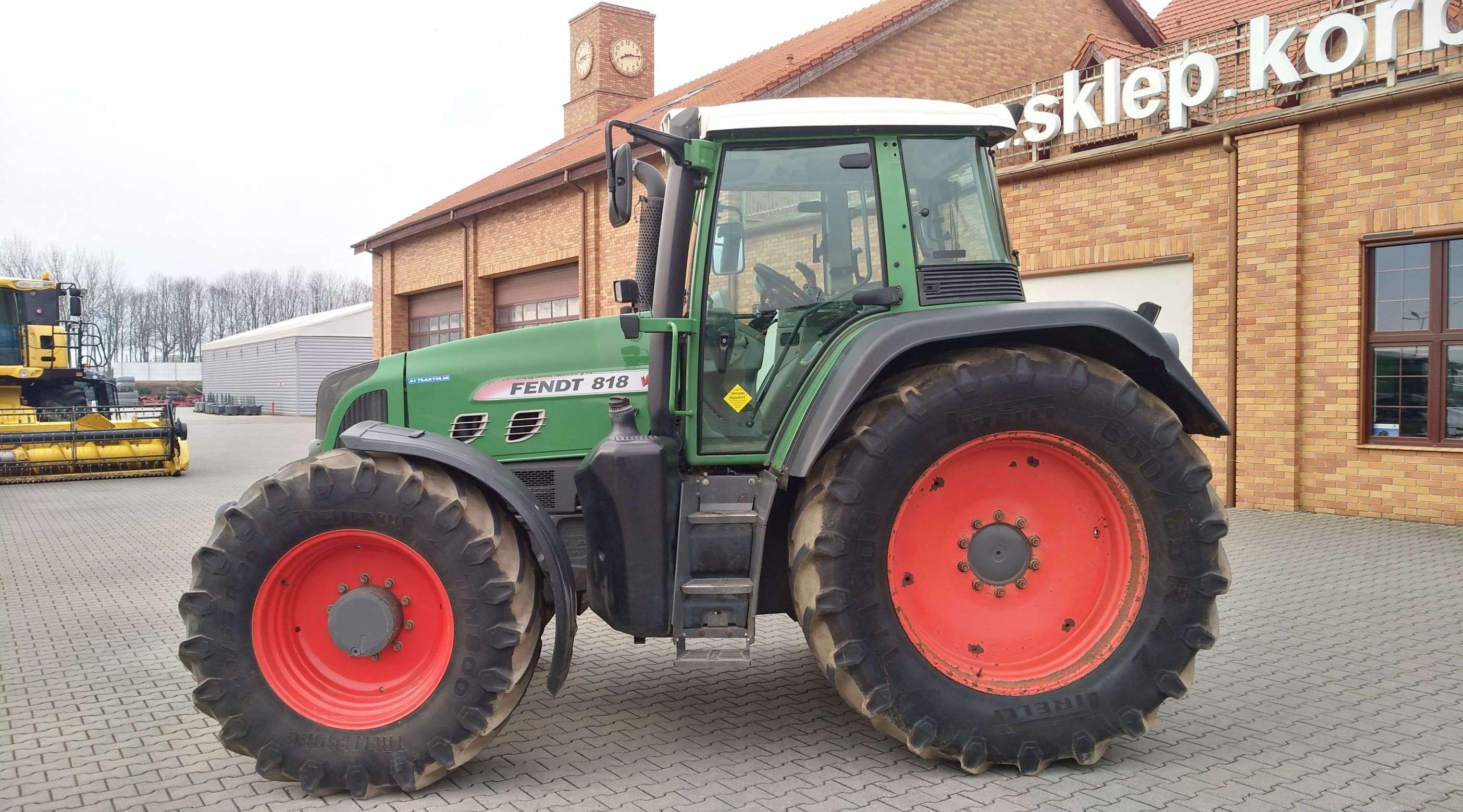 Ciągnik Fendt 818 Vario TMS na tle magazynu części Korbanek widok lewego boku