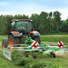 Czerwony traktor rolniczy zagrabia skoszoną koniczynę z trawą na łące za pomocą zielonej zgrabiarki zawieszanej Z-410 Samasz www.korbanek.pl