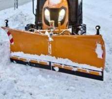 Pomarańczowy spychacz do śniegu City firmy Samasz zaczepiony do ciągnika komunalnego odśnieża chodnik