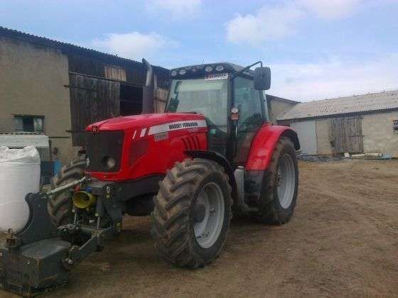 Widok na przód i bok ciągnika marki Massey Ferguson model 5465 czerwony traktor stoi na tle budynku gospodarczego