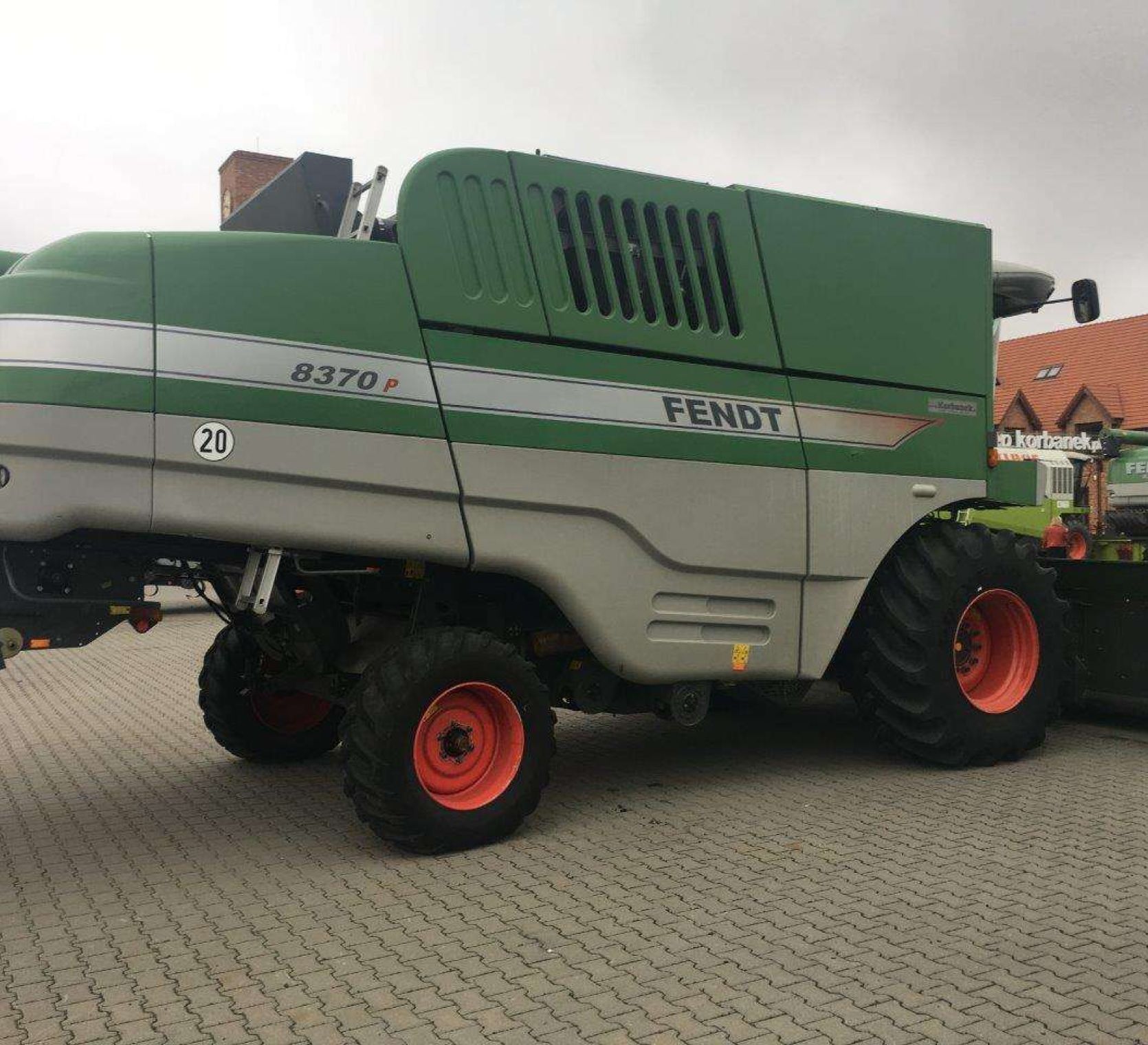 Używany Kombajn zbożowy FENDT 8370 P Kombajn używany FENDT 8370 P na utwardzonym placu w tle budynek z czerwonym dachem widok z prawego boku