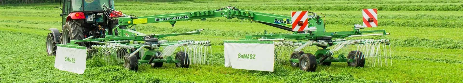 Zielona zgrabiarka zaczepiana 2-gwiazdowa DUO 680 firmy Samasz zaczepiona do czerwonego ciągnika zgrabia trawę na łące Korbanek.pl
