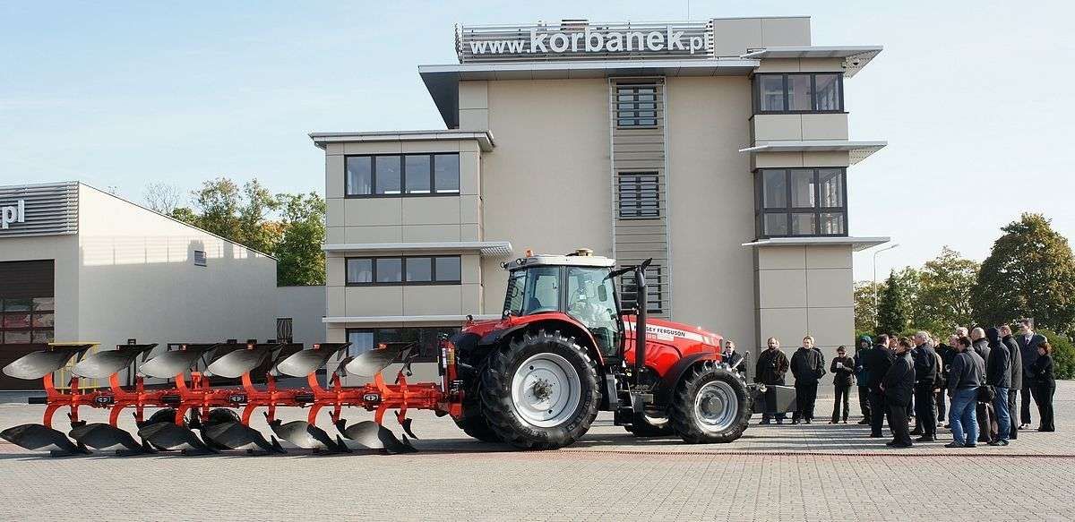 ciągnik rolniczy Massey Ferguson z pługiem obrotowym przed firmą korbanek przed nim grupa zainteresowanych osób